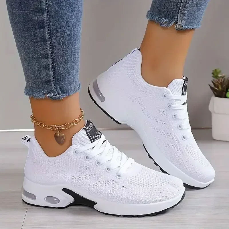 Witte ademende sneakers met mesh-bovenwerk, zwarte zoolaccenten en veters, gedragen met jeans en enkelbandje.