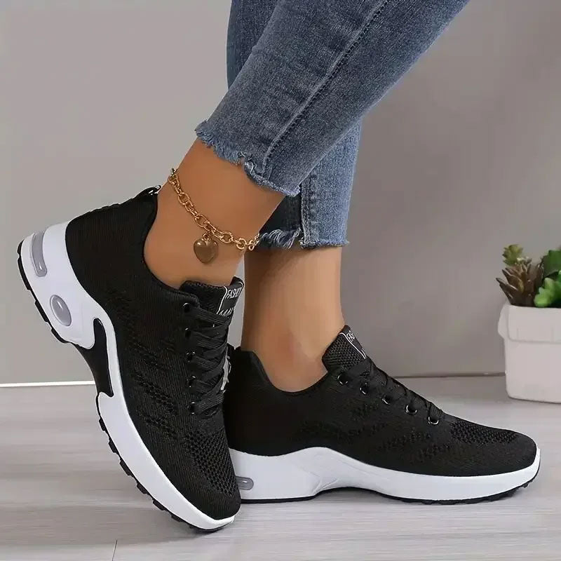 Zwarte ademende sneakers met mesh-bovenwerk, witte zool en veters, gedragen met jeans en enkelbandje.