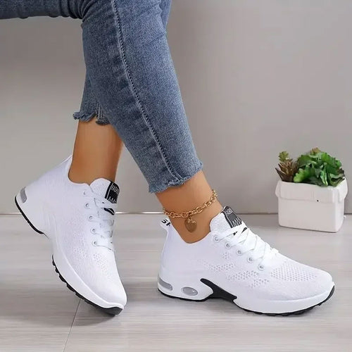 Witte ademende mesh sneakers met zwarte accenten en dikke zool, gedragen met jeans en enkelbandje.