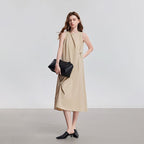 Model draagt een beige mouwloze midi jurk met ronde hals, getailleerde pasvorm en decoratieve knopen.