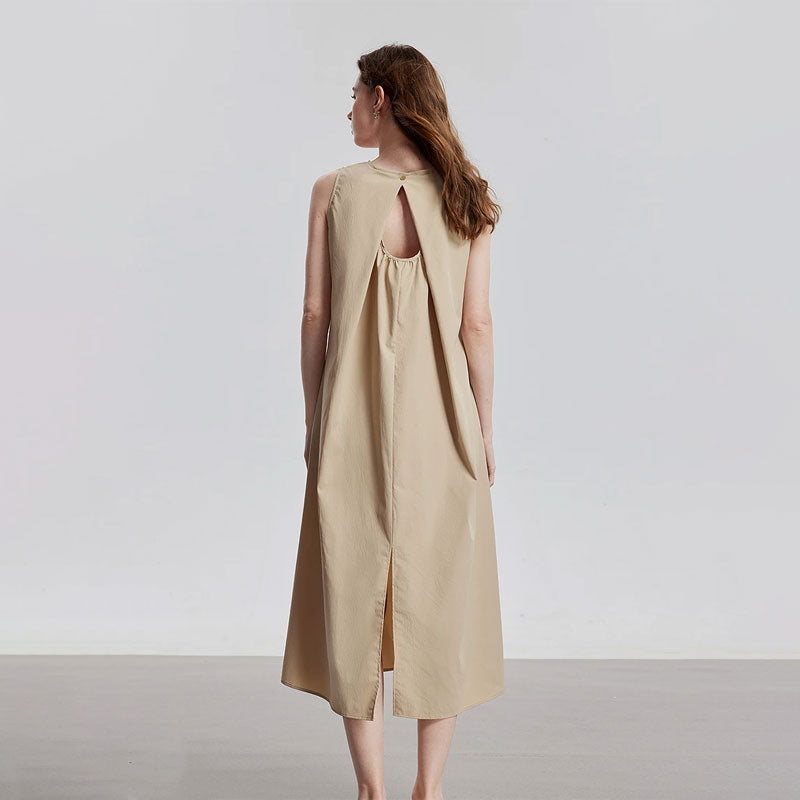 Vrouwelijke model draagt een beige mouwloze midi jurk met ronde hals en open rugdetail.