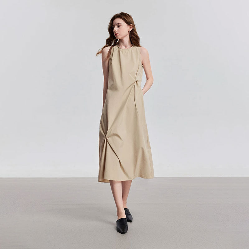 Model draagt een beige mouwloze midi jurk met ronde hals en gedrapeerde details.