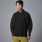 Man draagt een donkergroen geplooid poloshirt met lange mouwen en losse pasvorm, gecombineerd met gele broek.