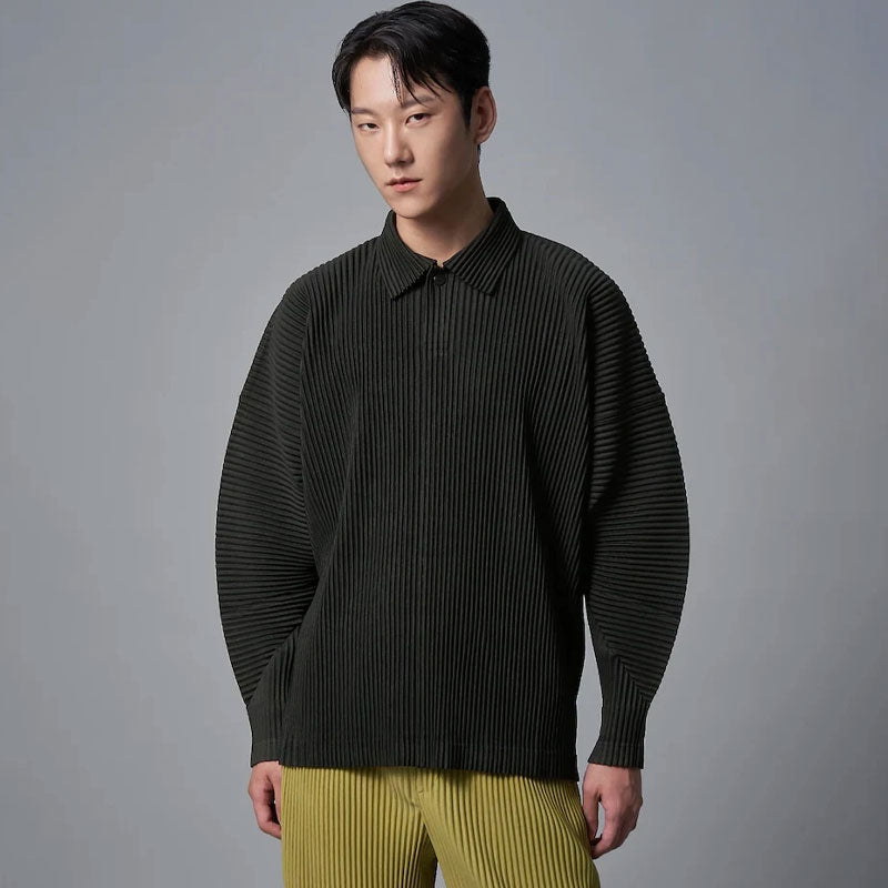 Man draagt een donkergroen geplooid poloshirt met lange mouwen en losse pasvorm, gecombineerd met gele broek.