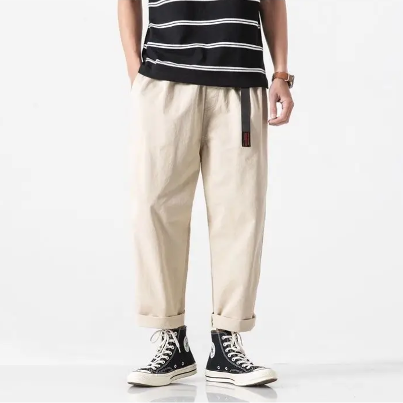 Beige katoenen wide leg cargo broek met elastische taille en zwarte riem, gedragen met sneakers.