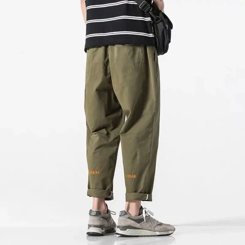 Man draagt comfortabele olijfgroene katoenen wide leg cargo broek met oranje tekst en opgerolde enkels.
