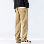 Beige losse rechte cargo jogger broek van katoenmix met elastische tailleband en klein geborduurd logo op de achterzak.
