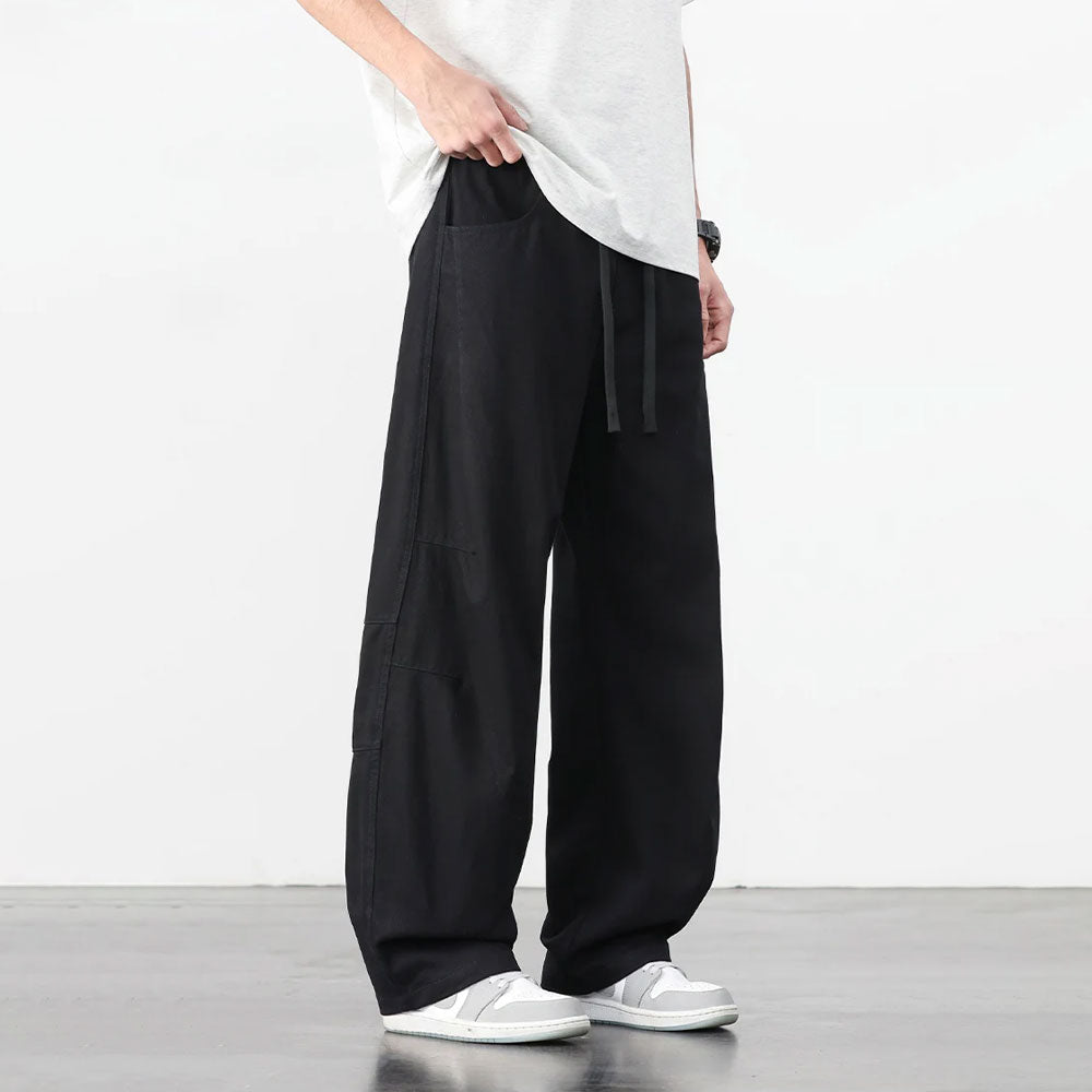 Zwarte retro katoenen workwear broek met losse pasvorm en trekkoord, gedragen met witte sneakers.