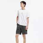 Man draagt wit T-shirt met subtiele gradient letterprint en donkergrijze shorts.